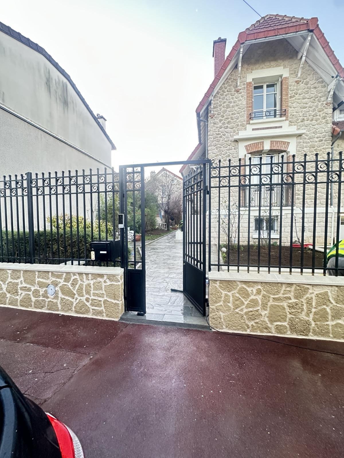 Maison en pierre derrière la clôture et le portail réalisés dans le même esprit